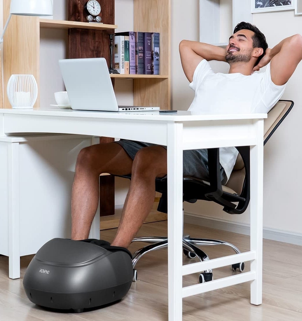A person sitting at a desk with their feet in the massager