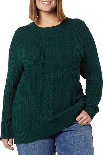 a model wearing a dark green fisherman cable knit sweater with blue jeasn