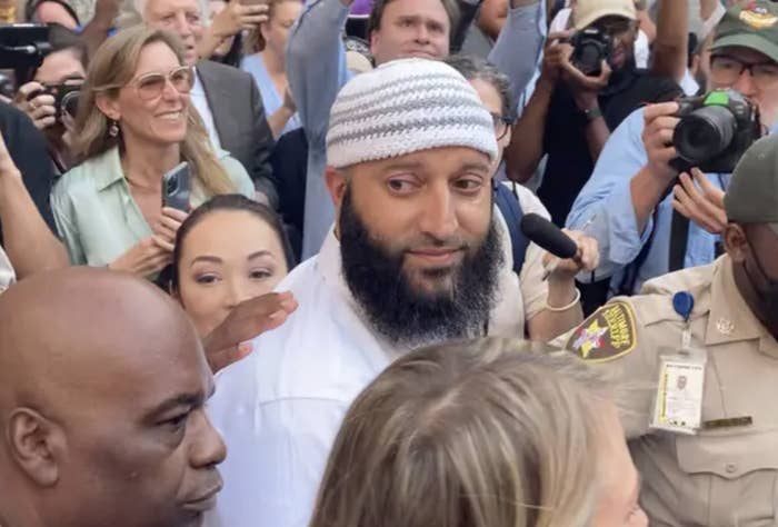 Adnan Syed looks on in a crowd of reporters with cameras