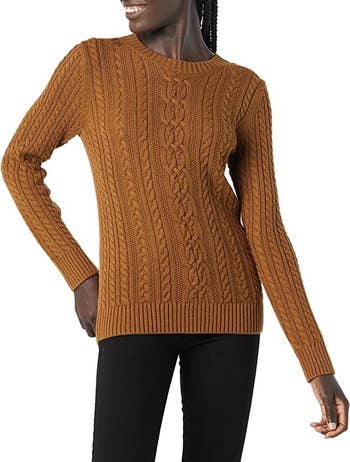 a model wearing a tan fisherman cable knit sweater with blue jeasn