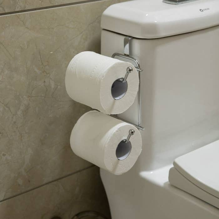 Two rolls of toilet paper on toilet paper holder on side of toilet