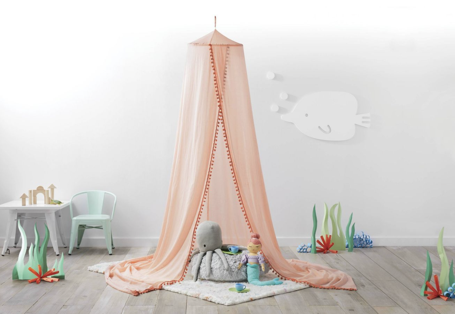 the light pink canopy with darker pink pom-poms on the opening in a child&#x27;s room