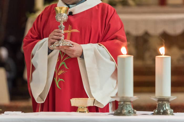 A priest holding a goblet in front of candles