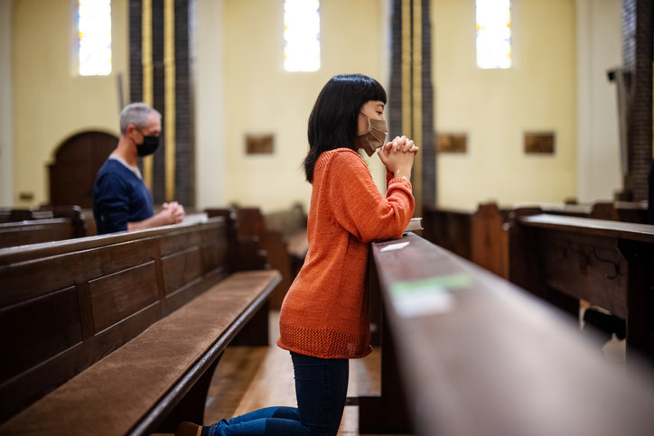 A young person kneeling in a church pew in prayer
