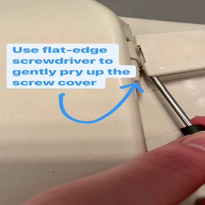 Someone using a flathead screwdriver to remove a toilet seat screw cover