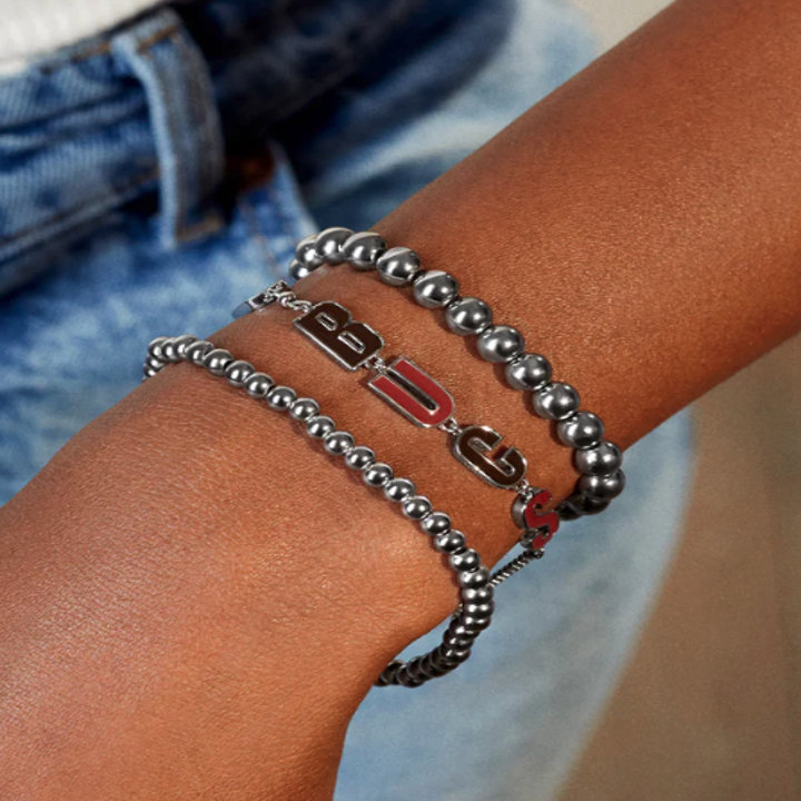 a model wearing a thin chain bracelet that says "go bucs" in red letters
