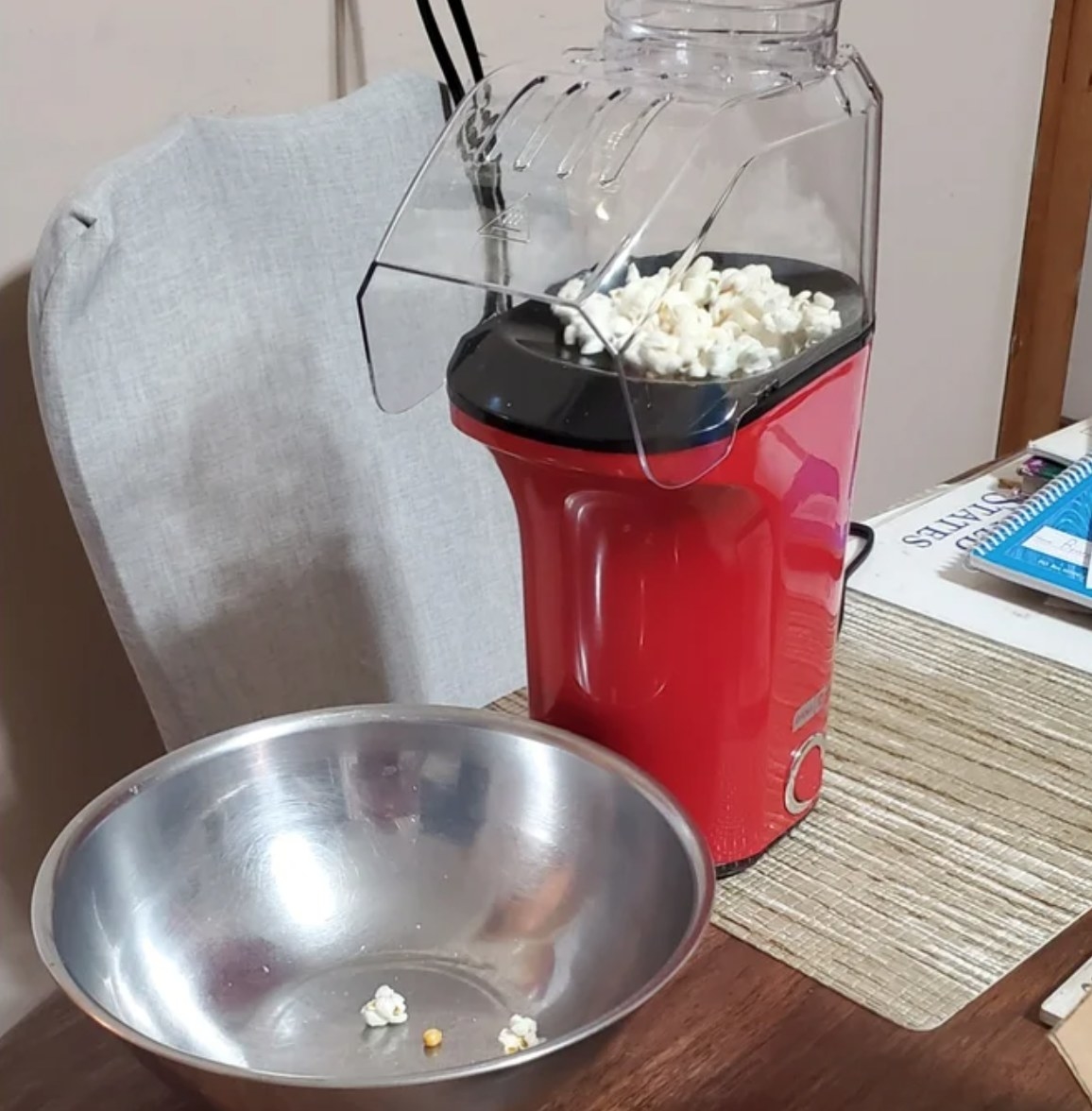 a red popcorn machine filled with fresh popcorn next to a metal bowl