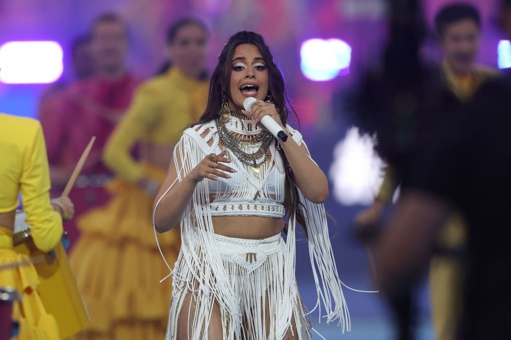 Camila wearing a tassled two-piece outfit and singing into a microphone