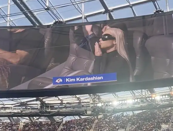 Kim wearing large sunglasses and blowing a kiss on the Jumbotron