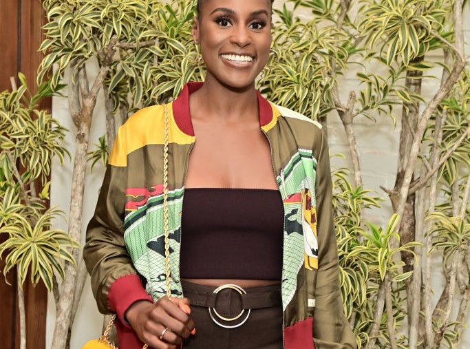 Issa smiling and wearing a colorful jacket while standing with a backdrop of foliage behind her