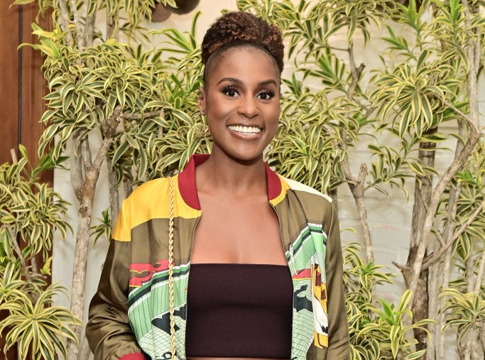 Issa smiling and wearing a colorful jacket while standing with a backdrop of foliage behind her