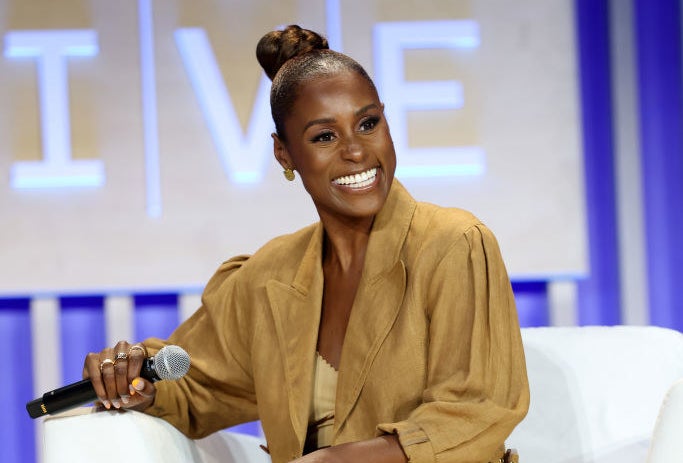 Issa sitting on a couch, smiling, and holding a microphone