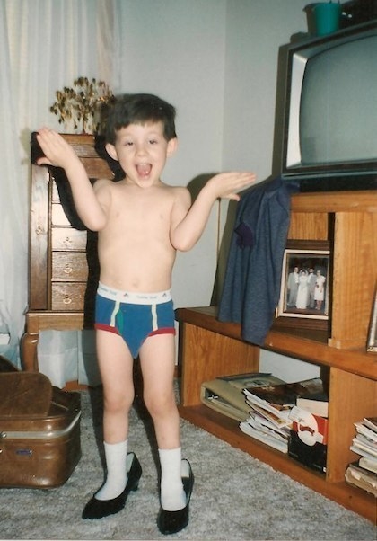 A young child with their hands raised, wearing briefs and high-heeled adult pumps
