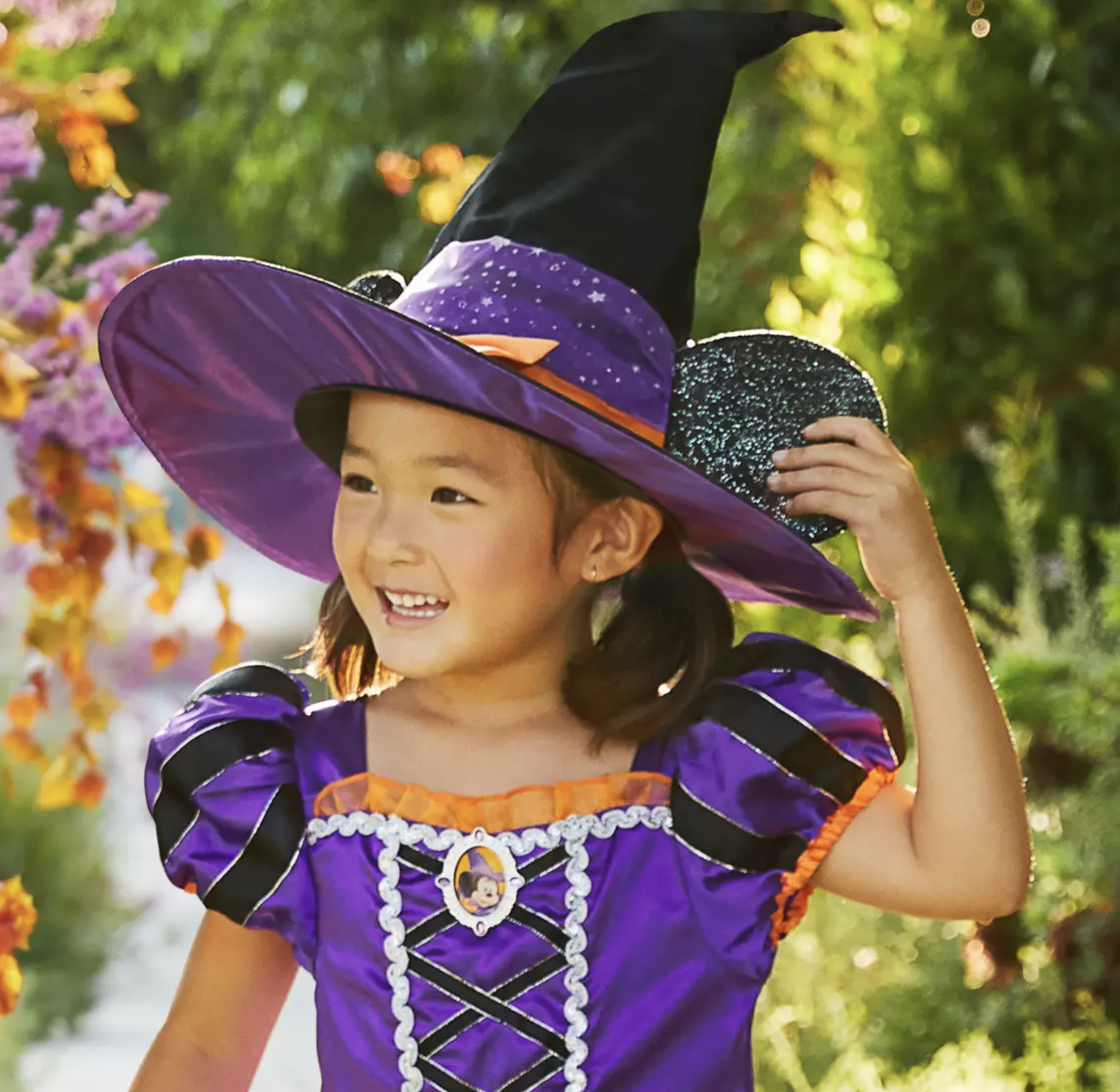 A child wearing a witch costume with a witch hat that has Minnie Mouse ears on the sides.