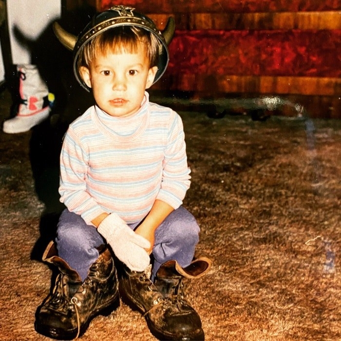 A child crouching on a rug while wearing adult lace-up work boots
