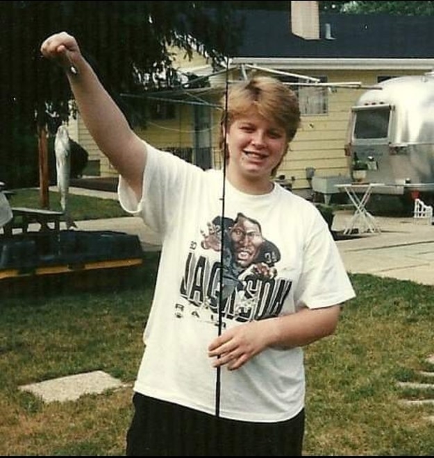 A young person with a mullet and a Jackson Raiders football T-shirt with their arm raised