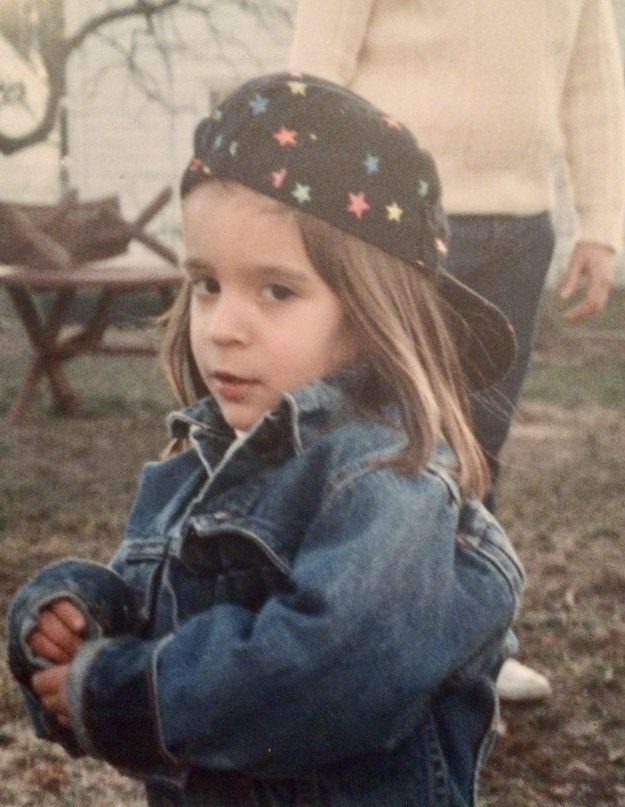 A young girl in a jean jacket and a backward baseball cap with stars on it