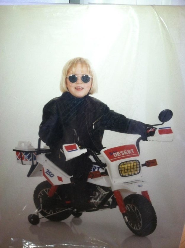 Smiling young child in a bomber jacket sits on a motorcycle and wears sunglasses