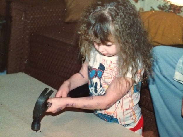 A young child with long hair and wearing a Mickey Mouse T-shirt hammers a nail into a surface
