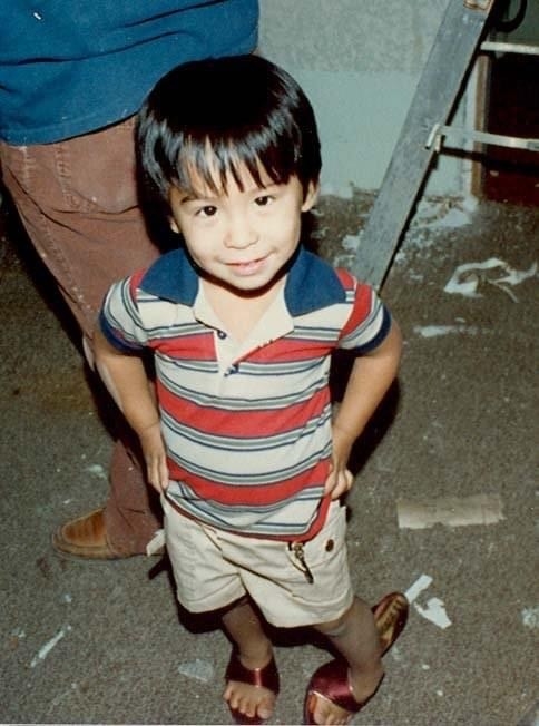 A young child with their hands on their hips and wearing a striped T-shirt, shorts, and high-heeled adult open-toe, high-heeled sandals