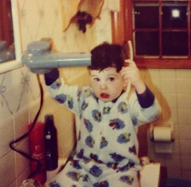 A young boy in pajamas in a bathroom using a blow-dryer