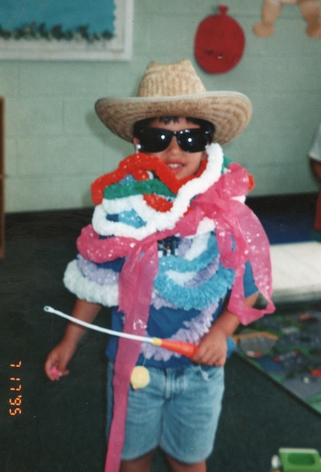A child wearing a large-brimmed straw hat, sunglasses, and many festive garlands around their neck