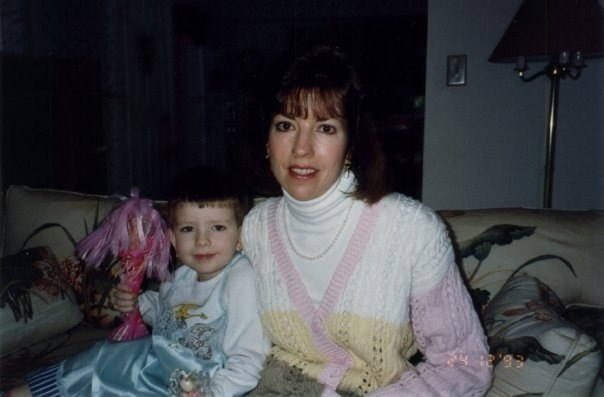 A young child holding a Barbie and sitting on a couch with a woman