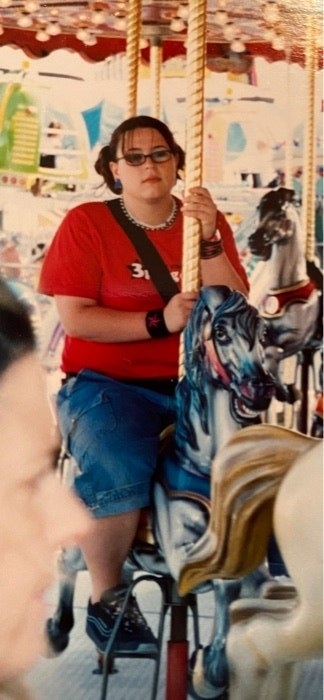 A young girl on a carousel wearing long jean shorts and a T-shirt