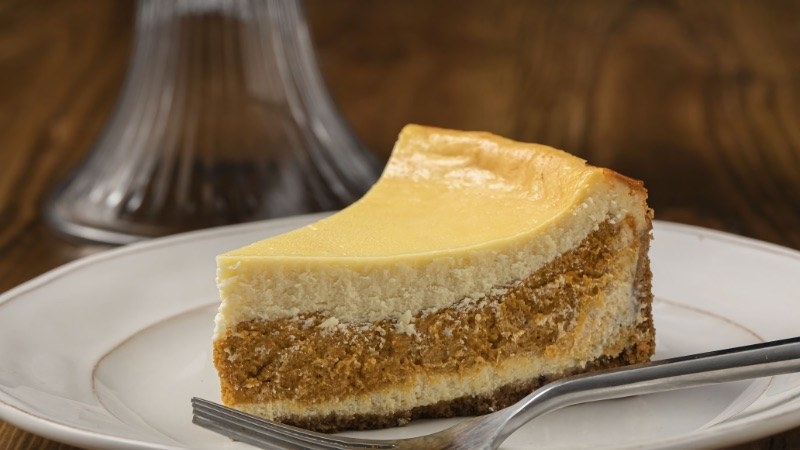 A slice of pumpkin cheesecake on a plate, with cheesecake on top and a pumpkin filling