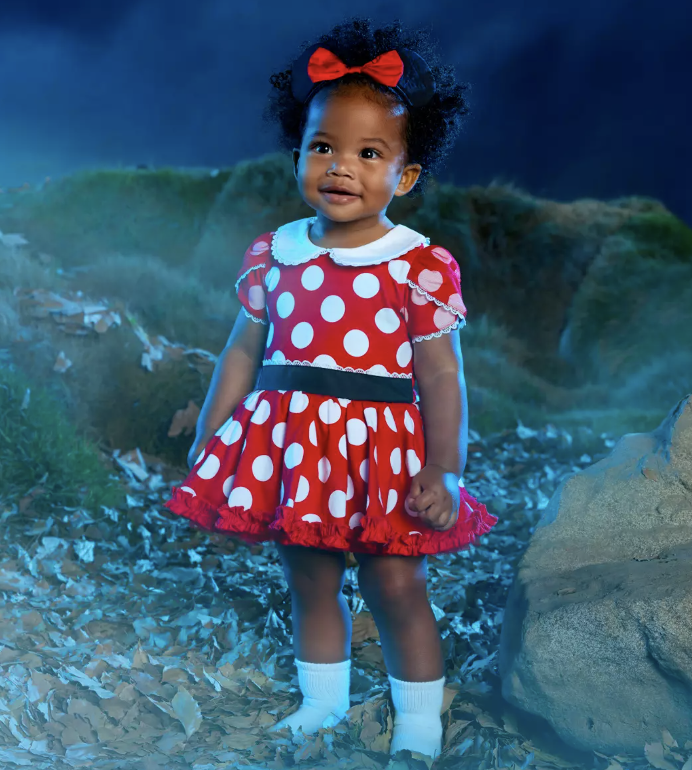 A child wearing a red Minnie Mouse costume with white polka dots and a red headband bow