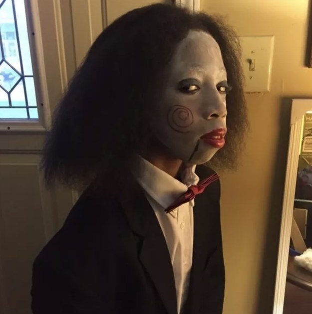 Someone dressed in a suit and bowtie with face paint that makes them look like Jigsaw from the &quot;Saw&quot; franchise