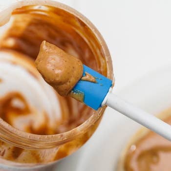 The spatula scraping up a bunch of PB from the edges of a seemingly empty peanut butter jar