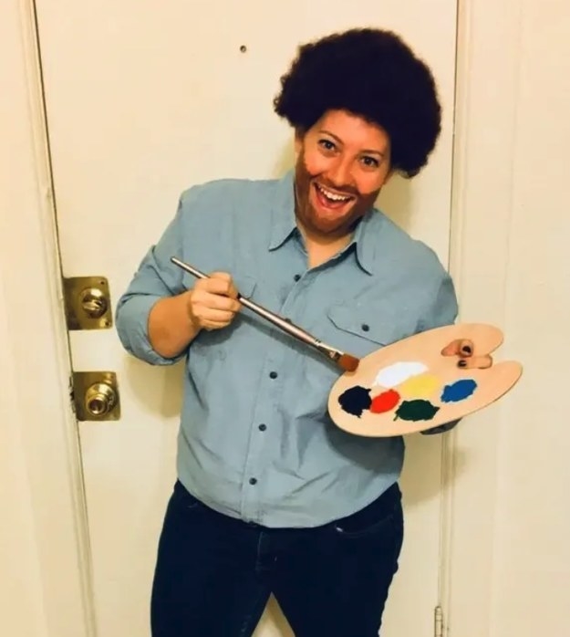 person in a black wig holding a paint set