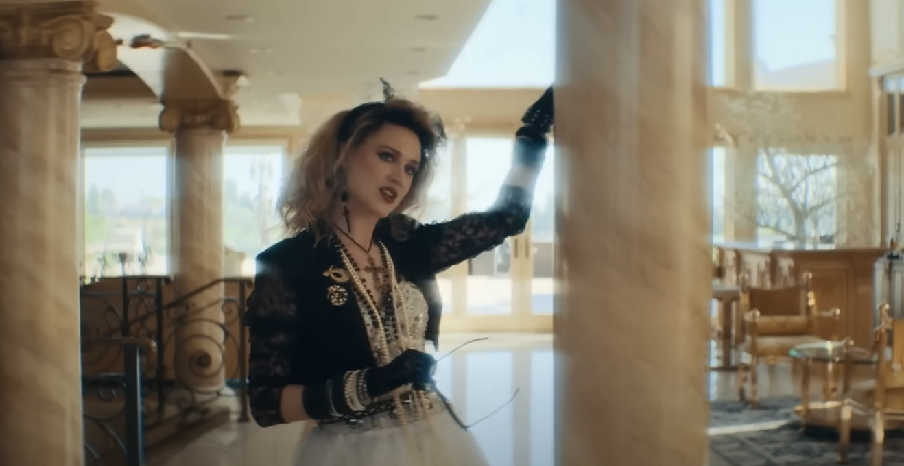Evan as Madonna standing next to a marble column inside a mansion