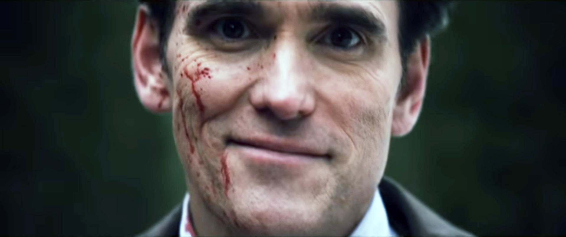 A man covered in blood smiles at the camera
