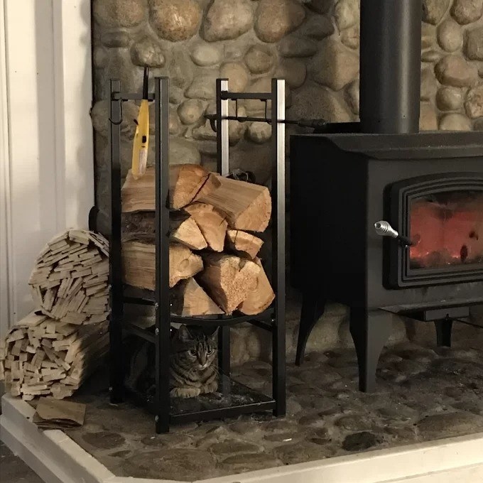 the log rack with a cat laying inside next to a wood-burning stove