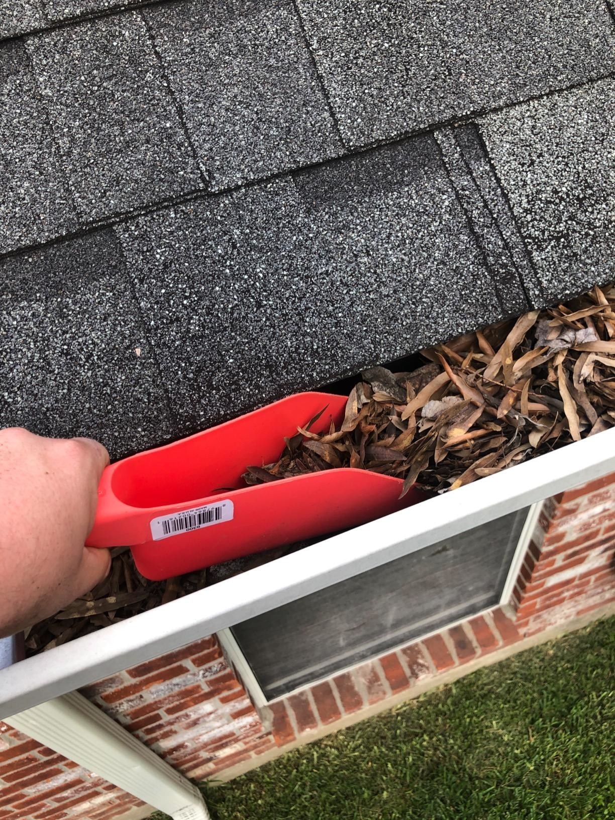 Reviewer using the red scoop to remove leaves from their gutter