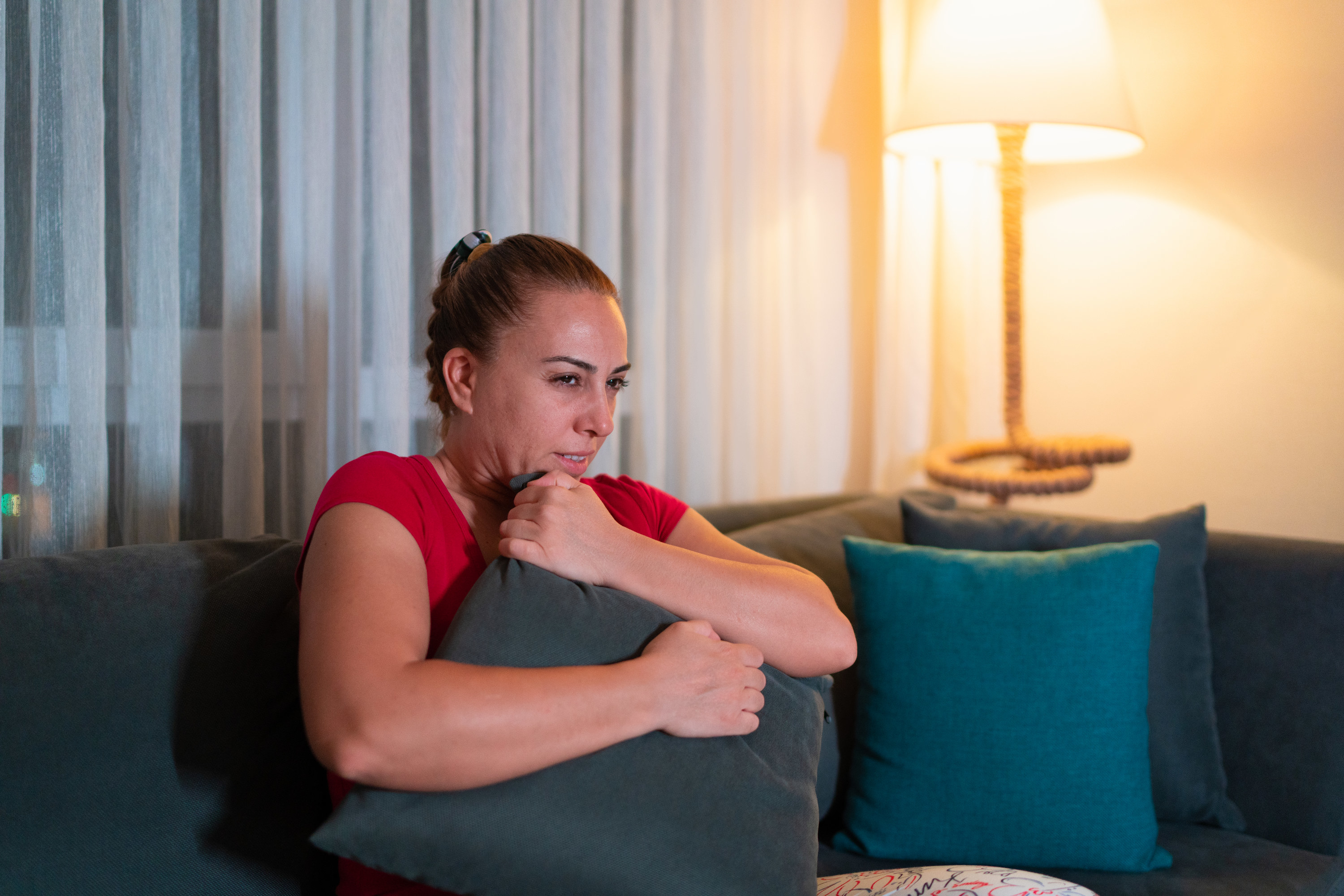 Woman hugging a pillow and wincing while watching something scary while sitting on a couch