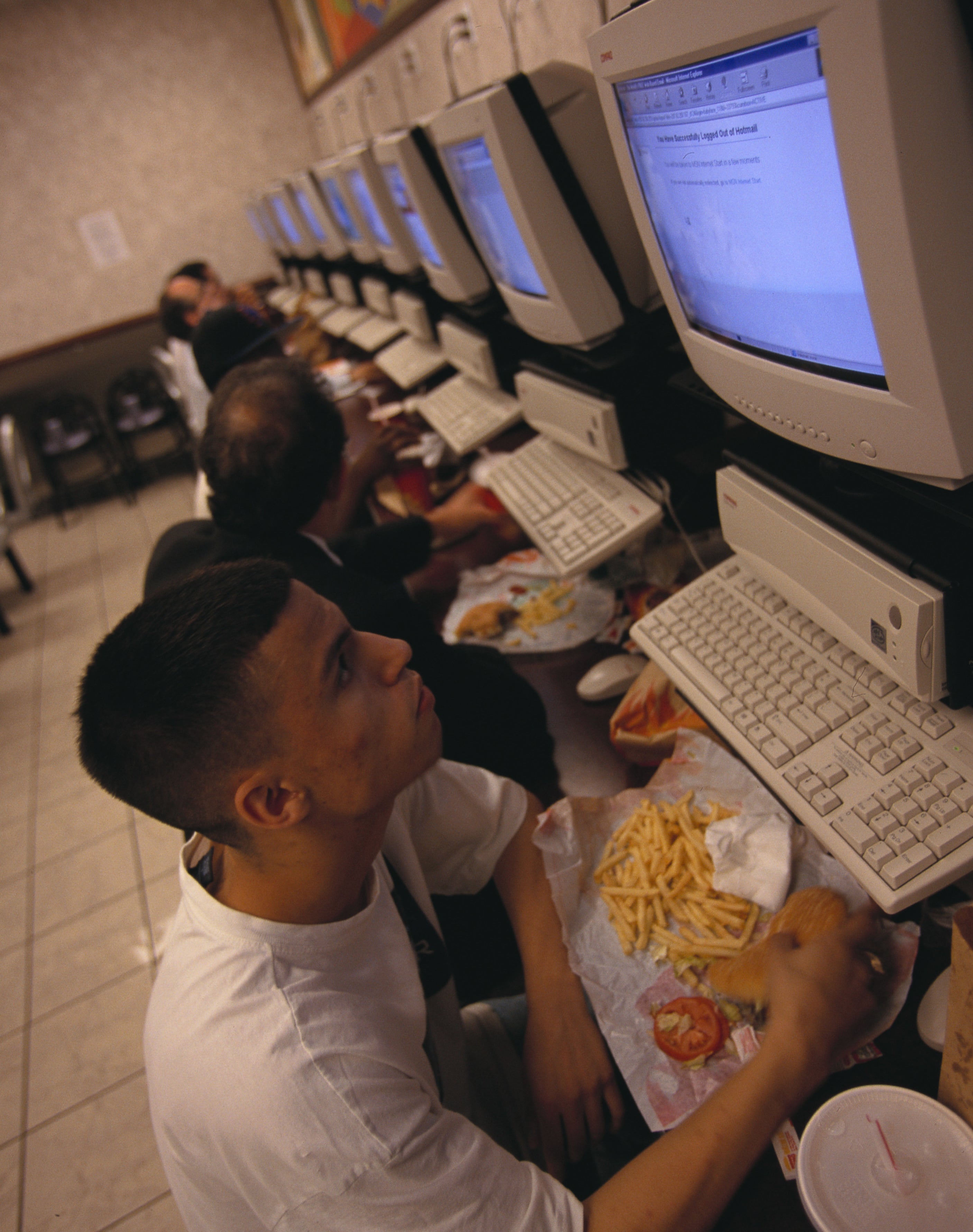 teen eating a burger and fries in front of a large 1990s desktop computer