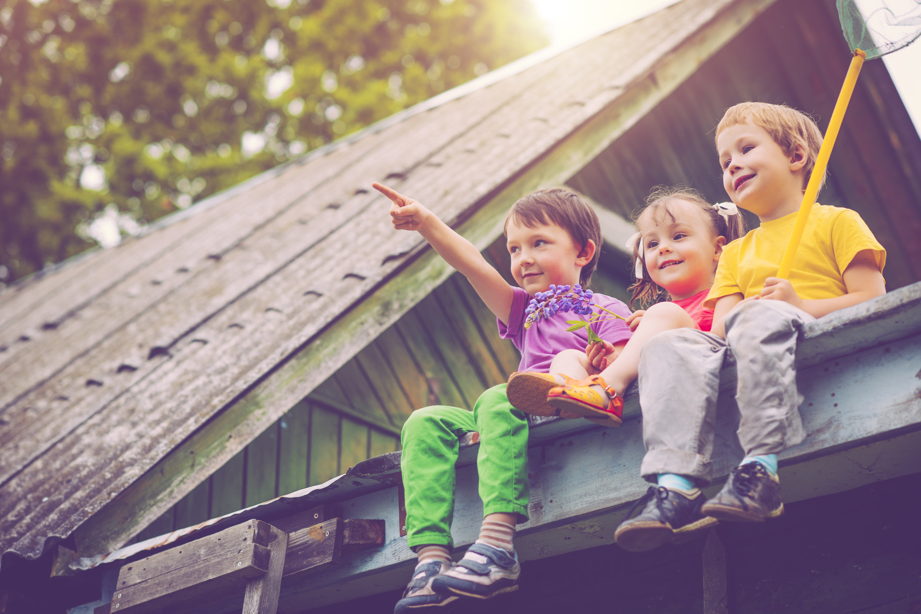 kids sitting on a roof together with their legs dangling over the side