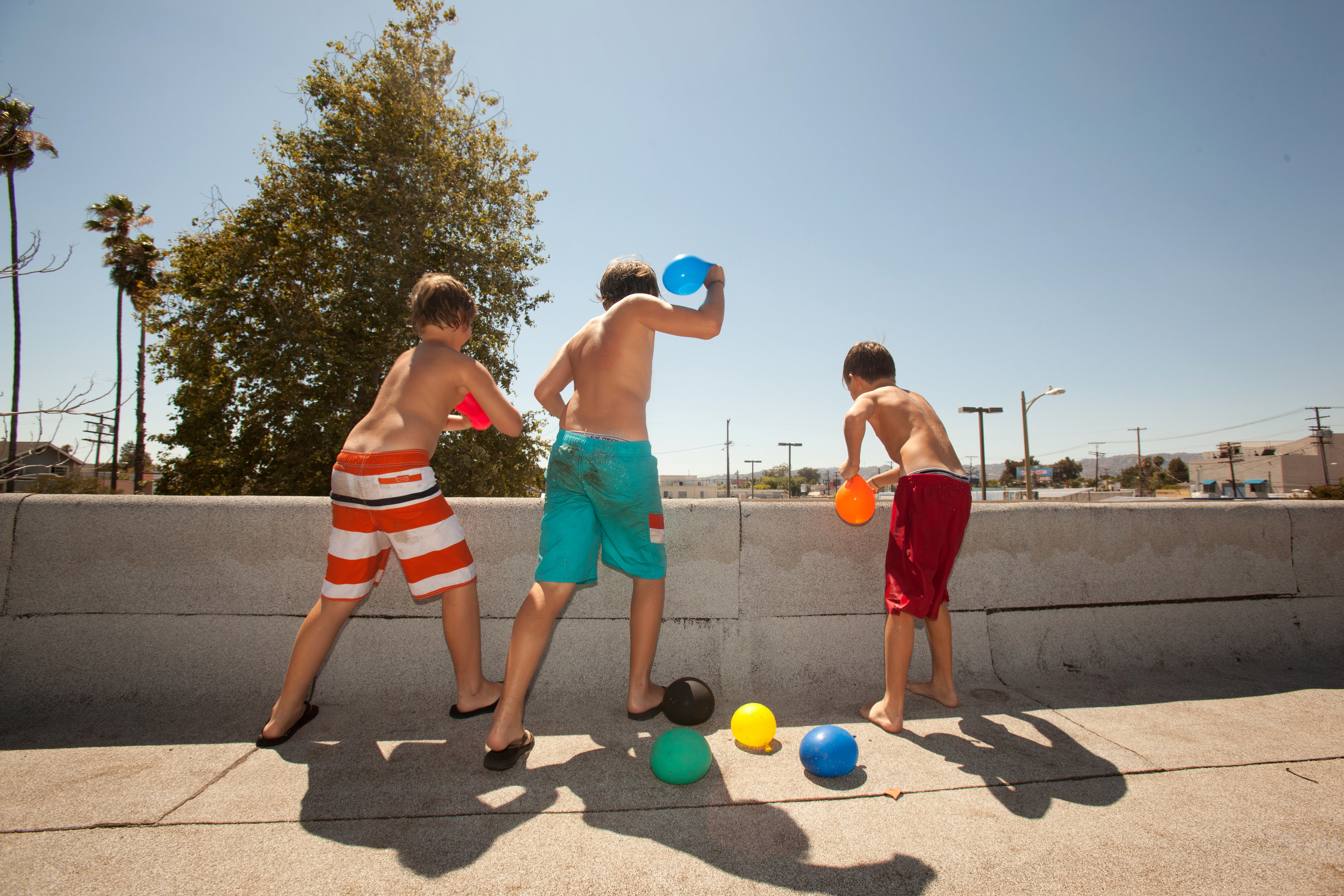 kids standing on a roof wearing swim trunks and throwing water balloons over the edge