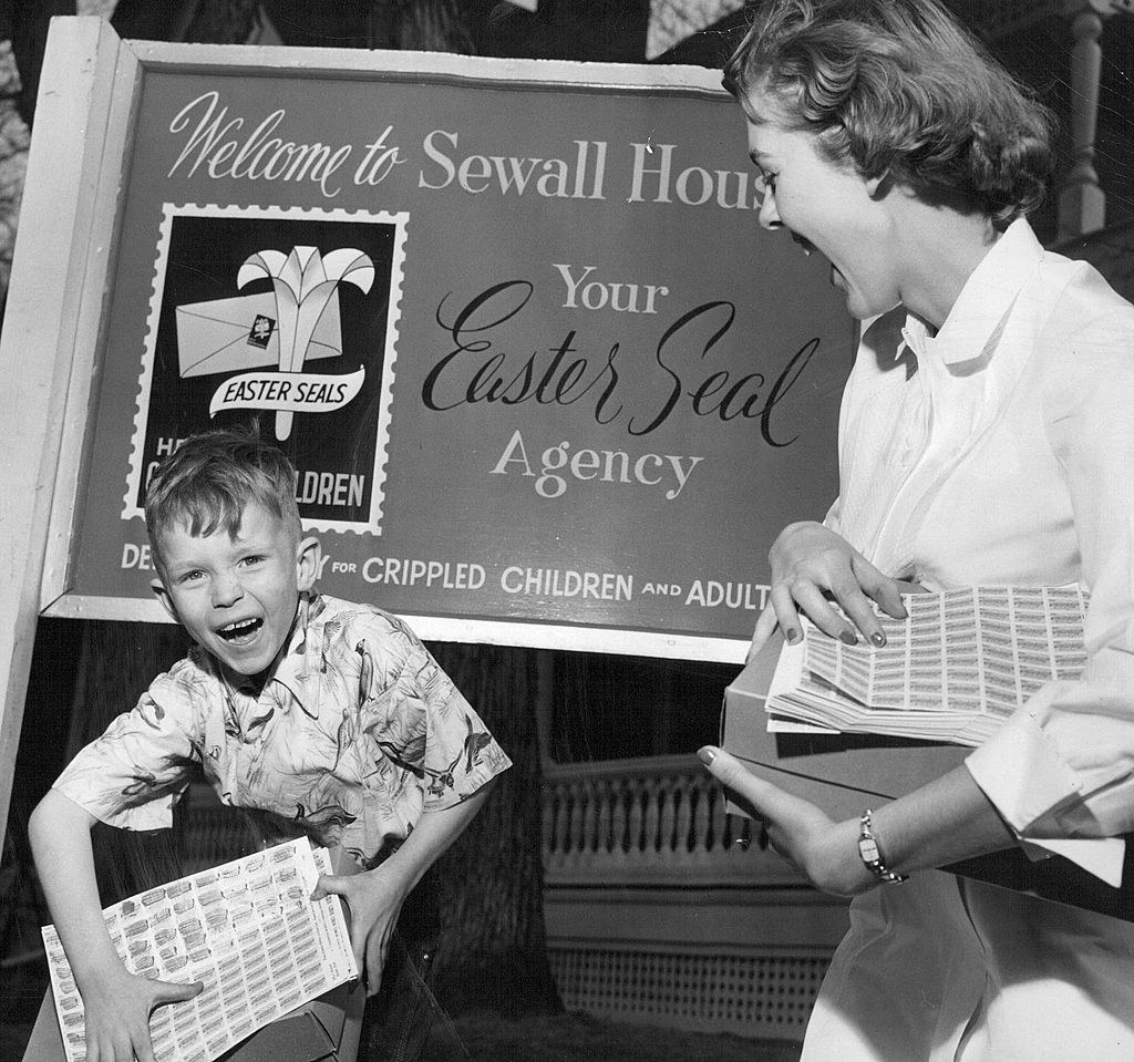 a young kid and teen holding stamps in front of a sign