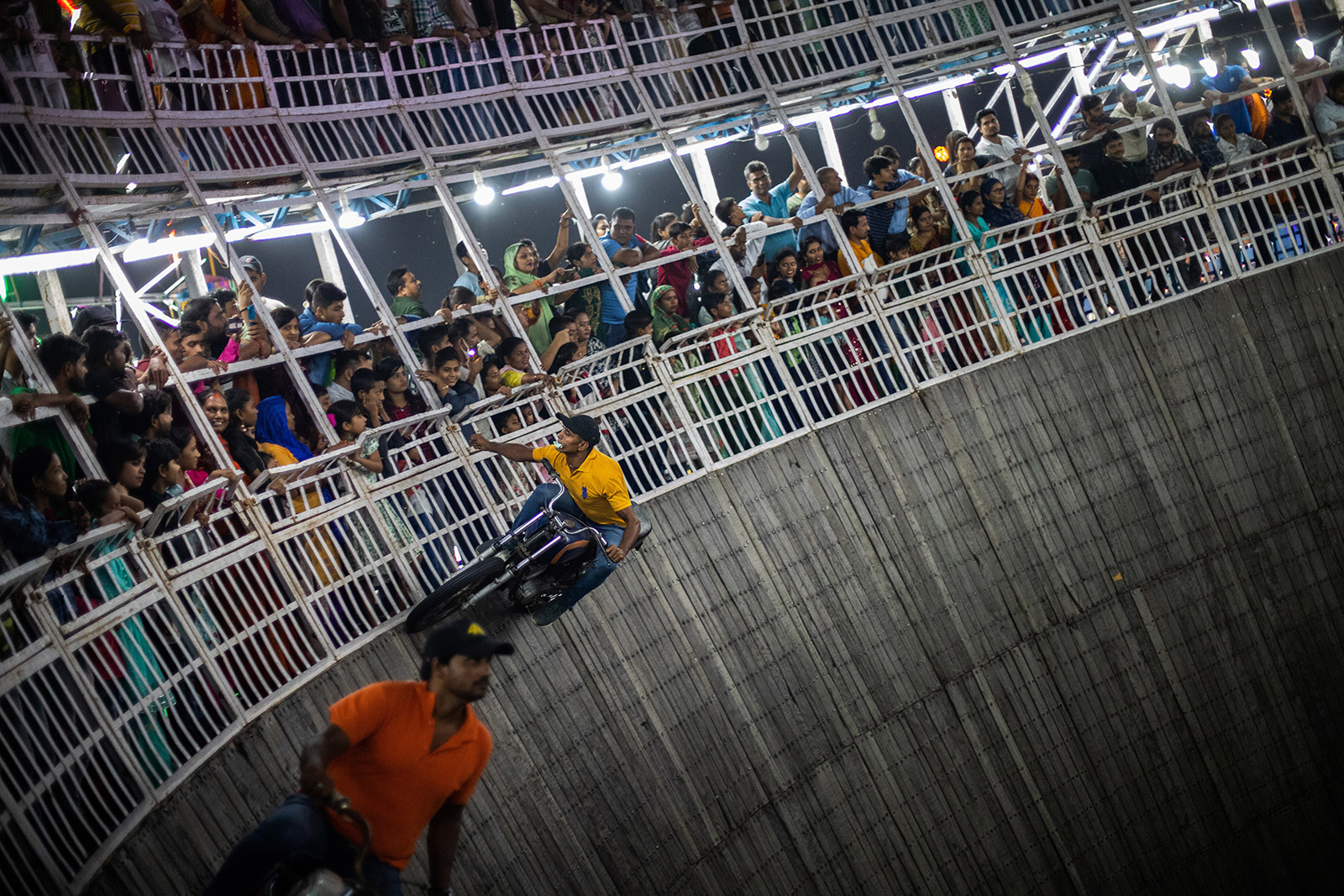 A man takes a tip from the audience as he drives on the top most area of the wooden cylindrical arena.