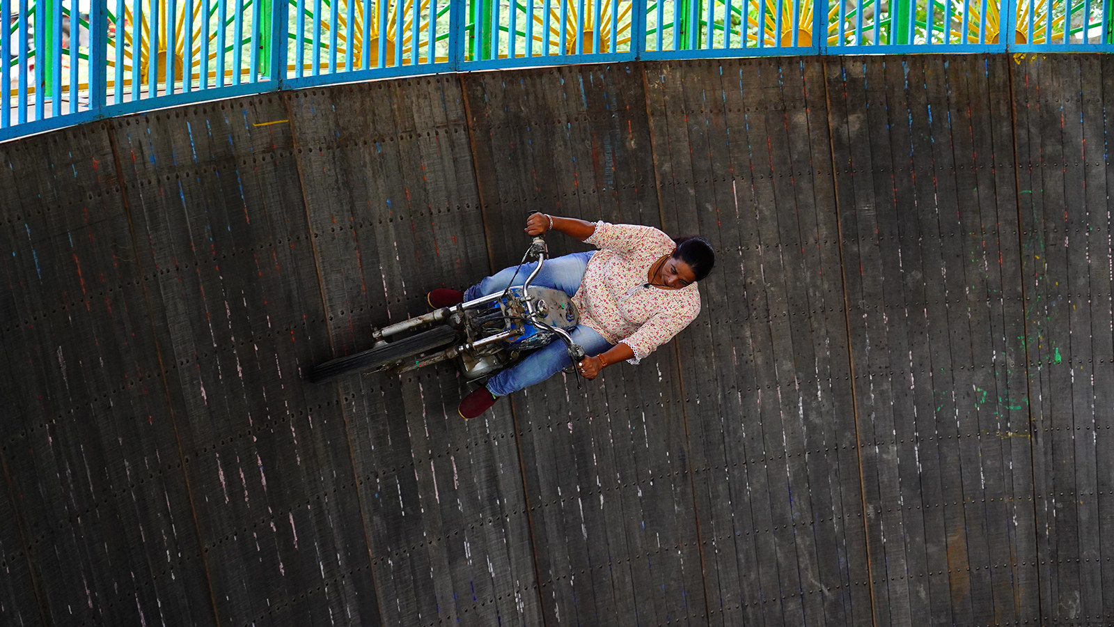 A woman rides a motorcycle in the &quot;Well of Death.&quot; She is vertical to the ground, using centrifugal force to stay on the wall.