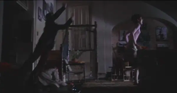 A man leaps from another room toward a woman