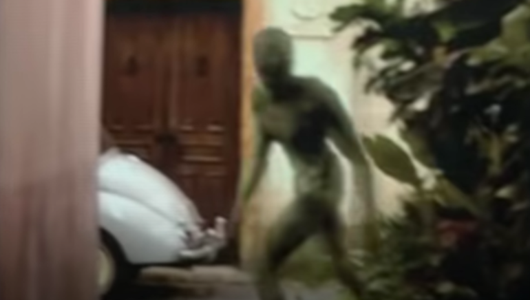 A alien walks out from behind a bush