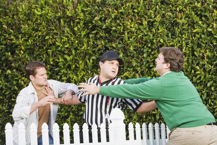 Two neighbors trying to fight over a picket fence with a referee in between attempting to keep them separated