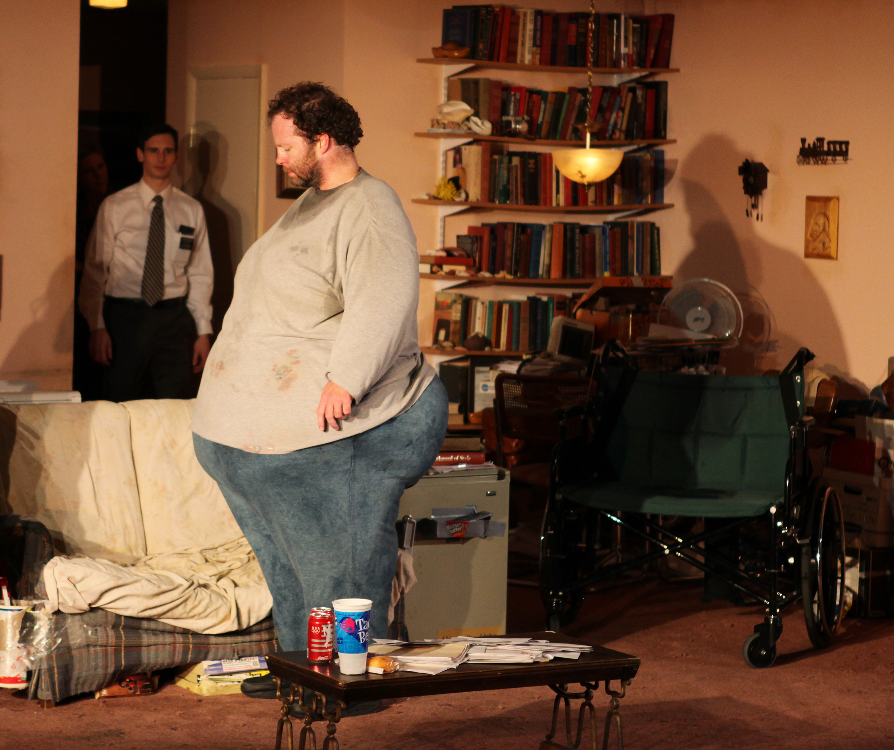 Charlie standing in the middle of his living room in a theater production of The Whale as someone stands in his doorway