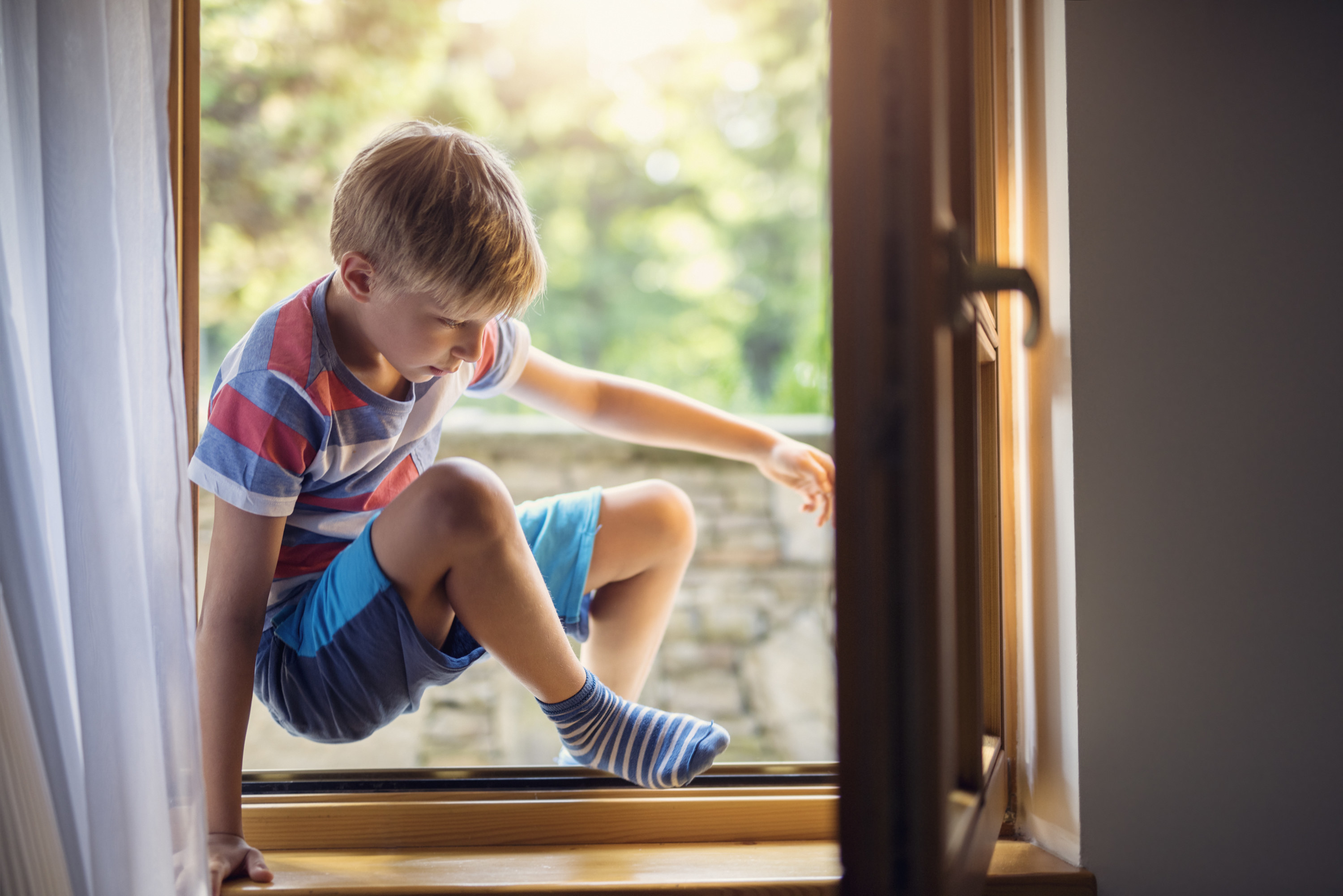 middle-school aged boy crawling into a window after being out of the house