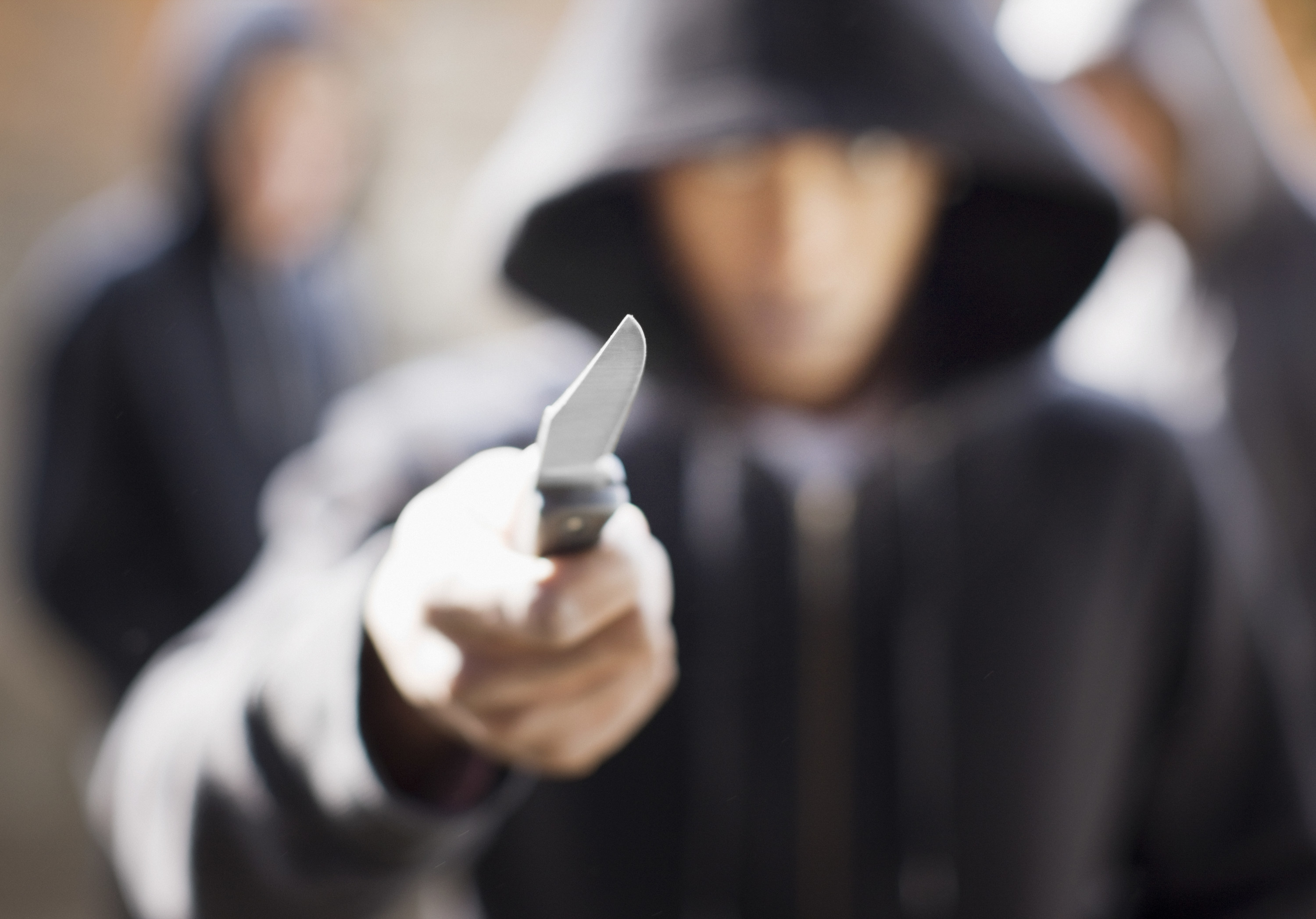 person in a black hoodie holding their arm out toward the camera with a knife in hand